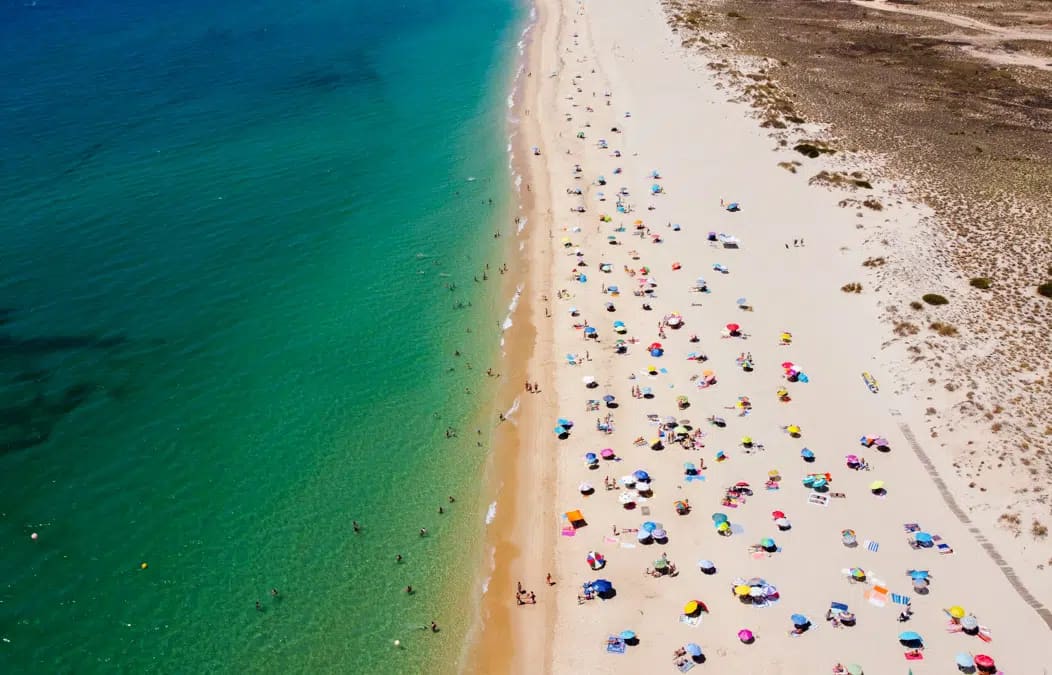 Aerial view of a long sandy beach with sunshades and clear green water