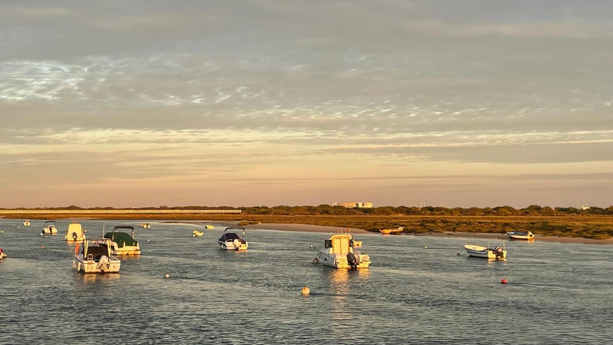 Small boats moored on the Ria Formosa lagoon at sunset, with the salt marsh beyond